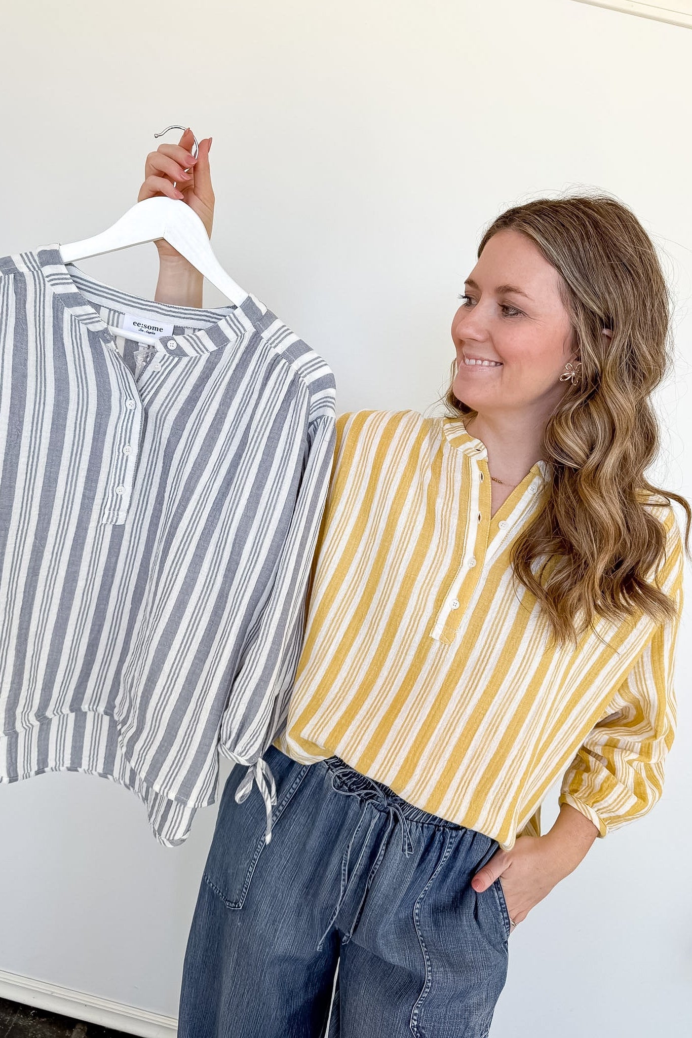 Woman holding a striped shirt on a hanger next to herself wearing a yellow and white striped shirt.