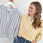 Woman holding a striped shirt on a hanger next to herself wearing a yellow and white striped shirt.