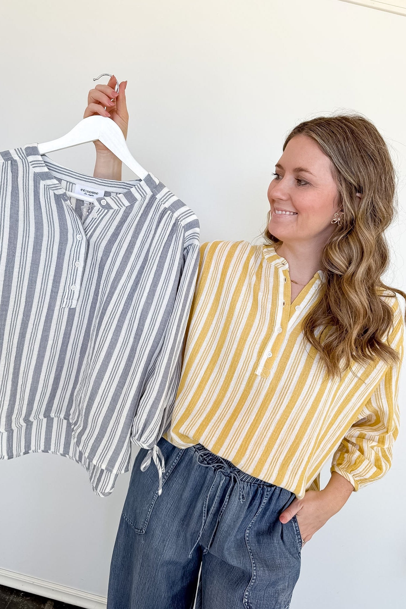 Woman holding a striped shirt on a hanger next to herself wearing a yellow and white striped shirt.