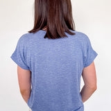 Person wearing a blue t-shirt and patterned pants against a white wall