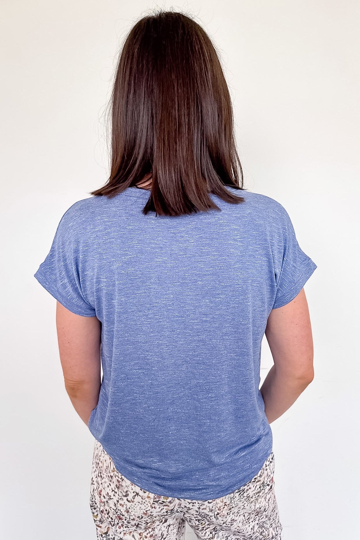 Person wearing a blue t-shirt and patterned pants against a white wall