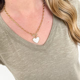 Person wearing a gold necklace with a heart pendant on a plain background