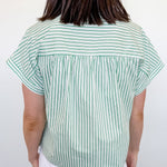 Person wearing a green and white striped shirt and white shorts against a plain background
