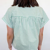 Person wearing a green and white striped shirt and white shorts against a plain background
