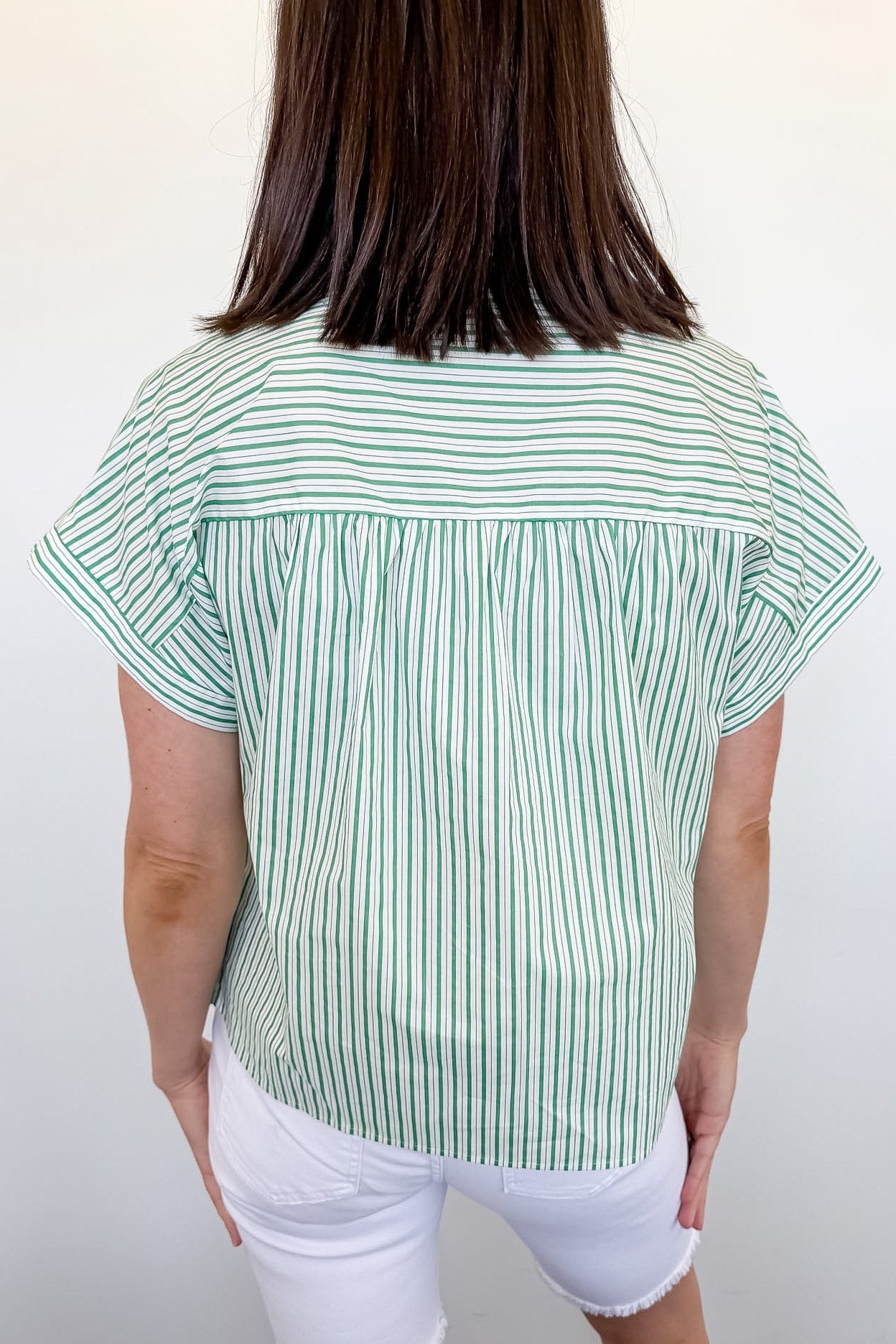 Person wearing a green and white striped shirt and white shorts against a plain background