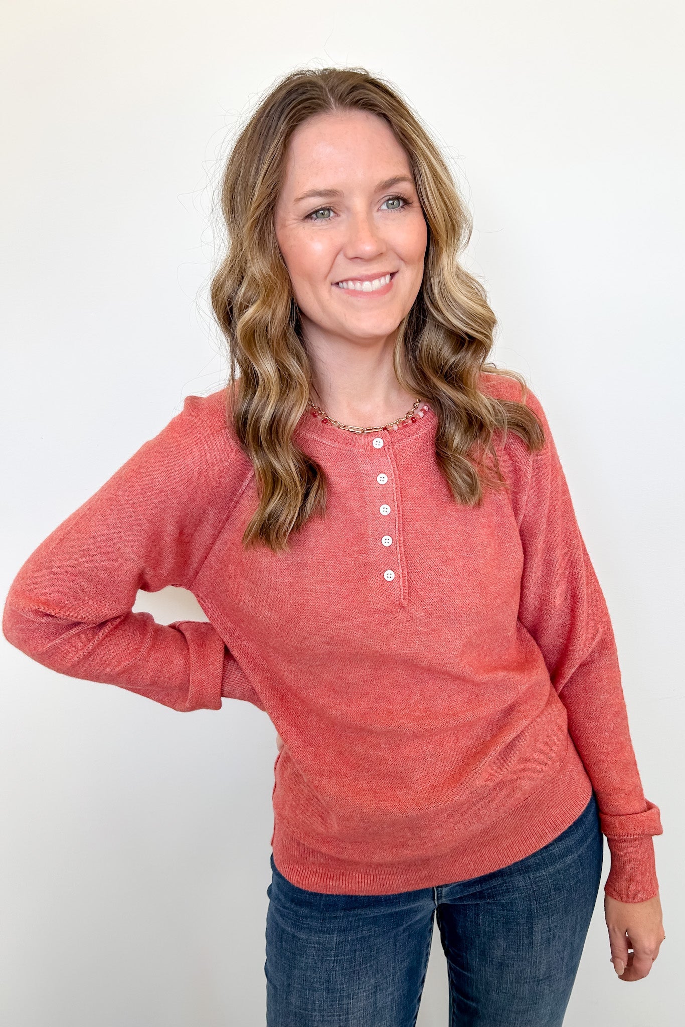 Woman wearing a red long-sleeve shirt and blue jeans against a white background