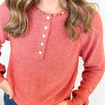 Person wearing a red long-sleeve henley shirt with white buttons on a plain background