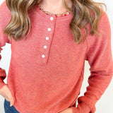 Person wearing a red long-sleeve henley shirt with white buttons on a plain background