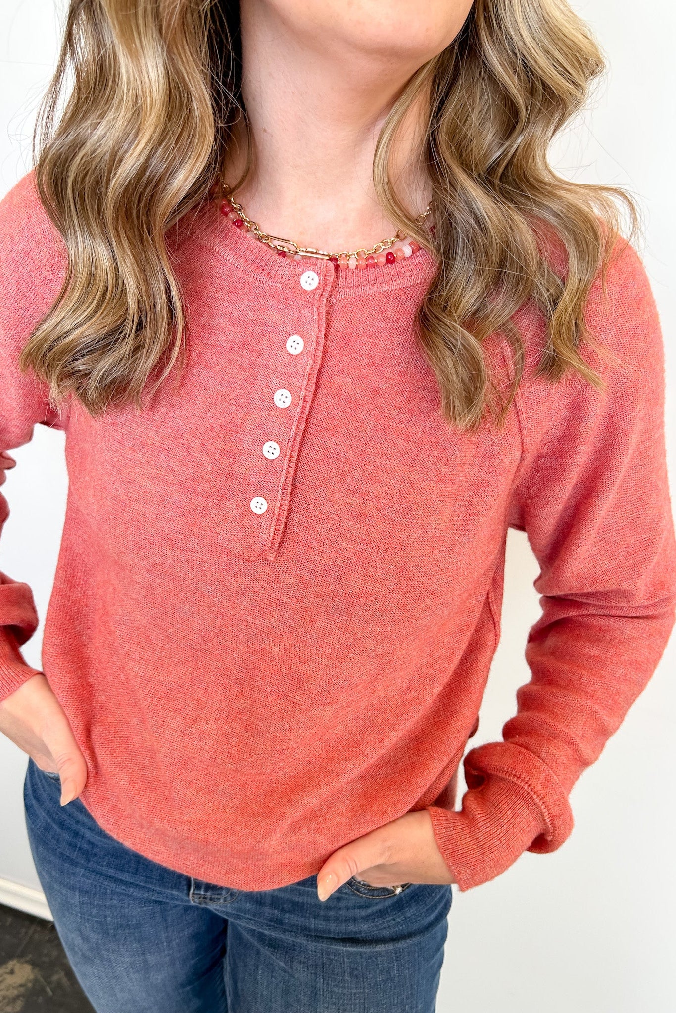 Person wearing a red long-sleeve henley shirt with white buttons on a plain background