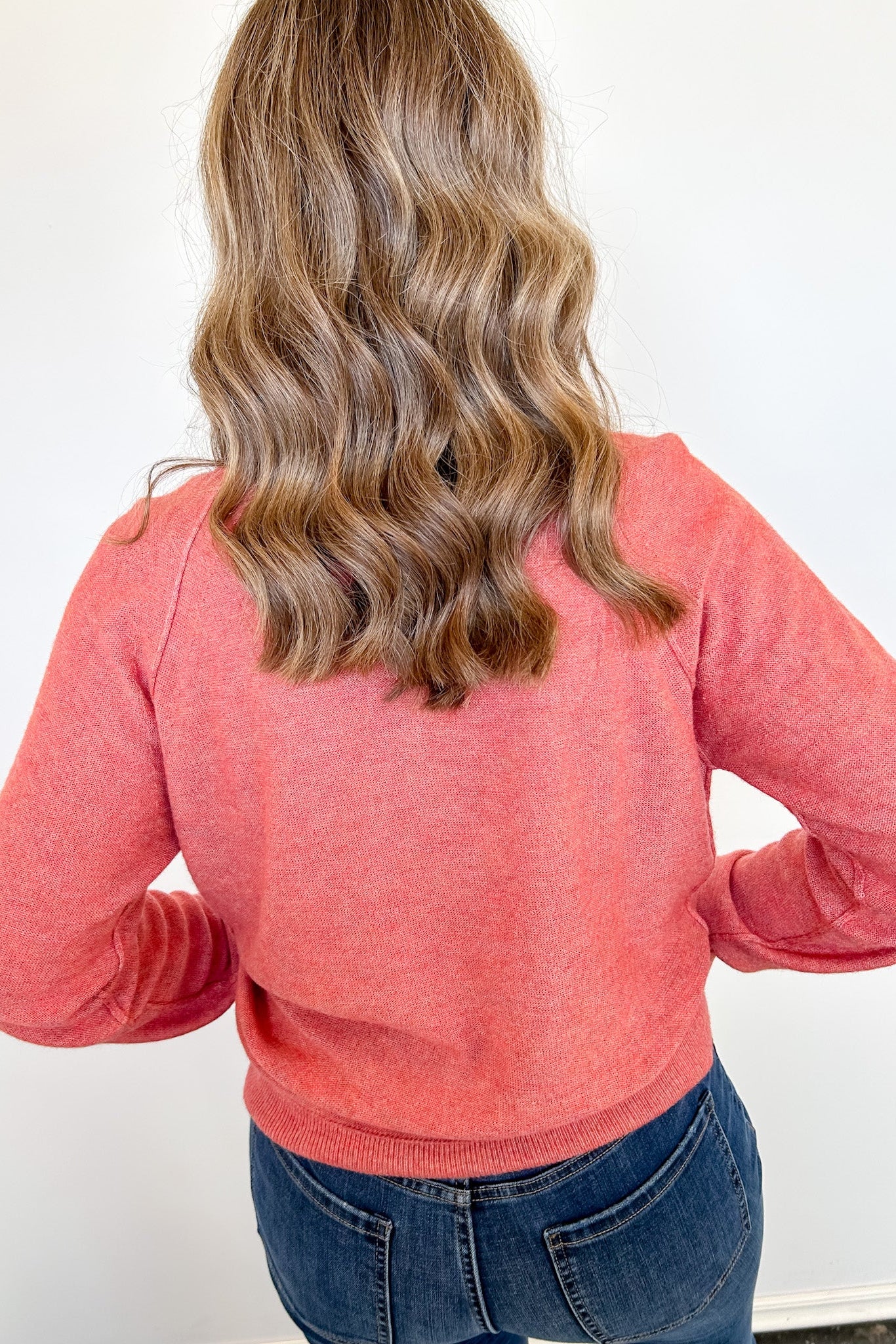 Person wearing a pink sweater and blue jeans against a white background