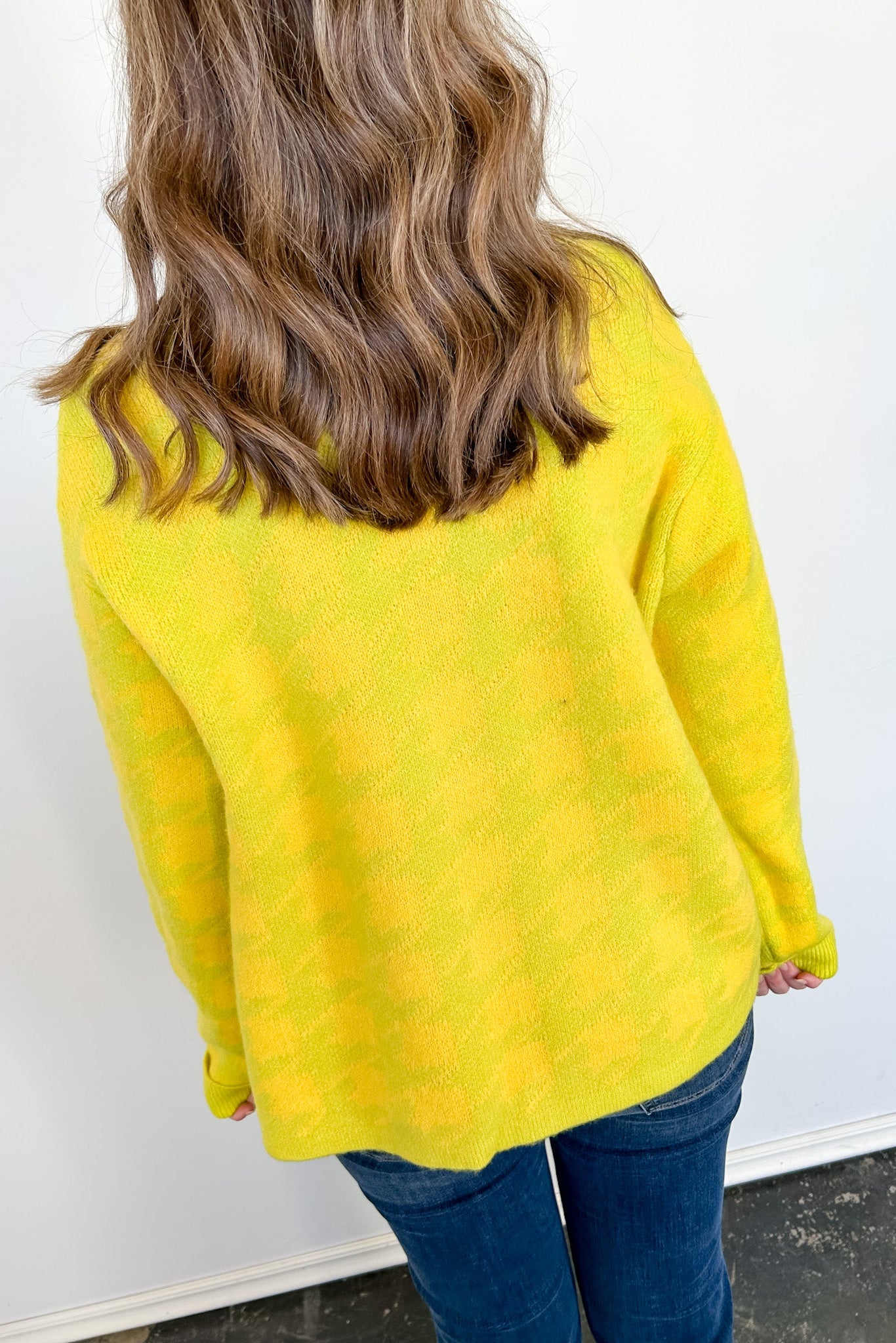 Person wearing a yellow sweater against a white wall