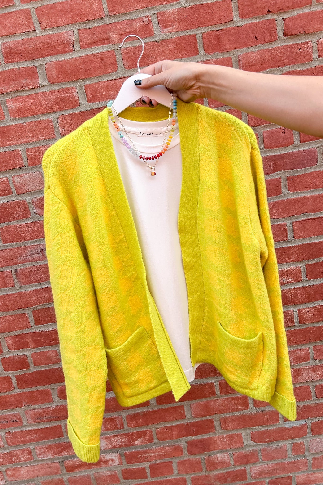 Yellow cardigan on a hanger against a red brick wall