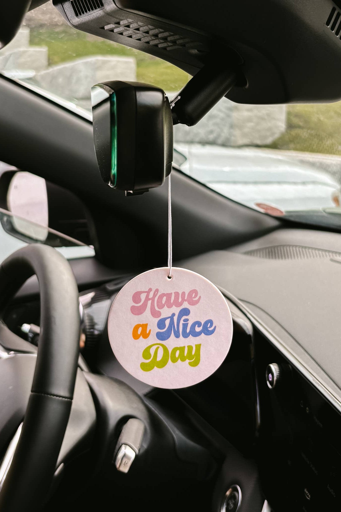 Car air freshener with 'Have a Nice Day' message hanging from a car's rearview mirror.