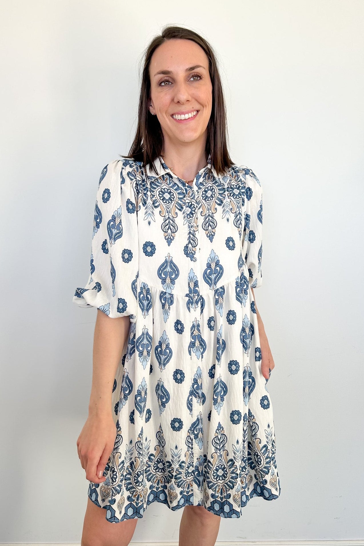 Woman wearing a white dress with blue floral patterns against a plain background