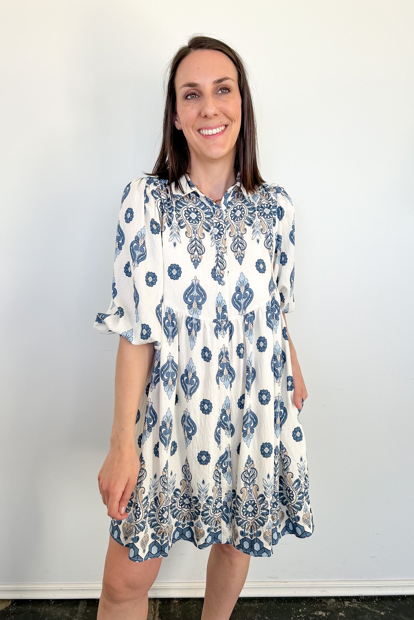 Woman wearing a white dress with blue floral patterns against a plain background