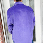 Person wearing a purple corduroy shirt standing in front of a door.
