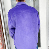 Person wearing a purple corduroy shirt standing in front of a door.