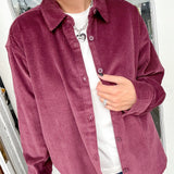 Person wearing a burgundy corduroy shirt over a white top and blue jeans indoors.