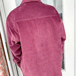 Person wearing a pink corduroy jacket standing in front of a glass door.