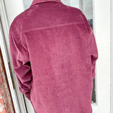 Person wearing a pink corduroy jacket standing in front of a glass door.