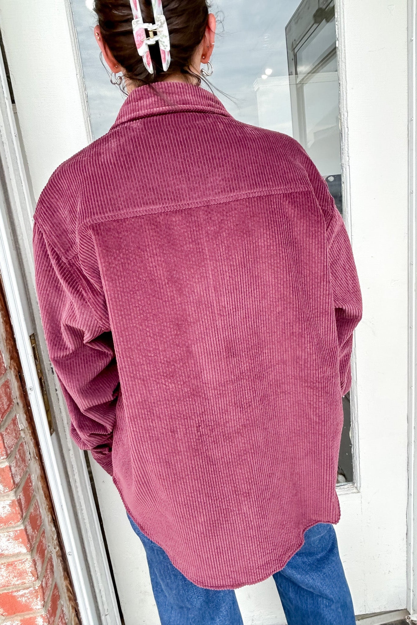 Person wearing a pink corduroy jacket standing in front of a glass door.