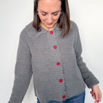 Woman wearing a gray cardigan with red buttons on a white background