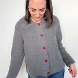 Woman wearing a gray cardigan with red buttons on a white background