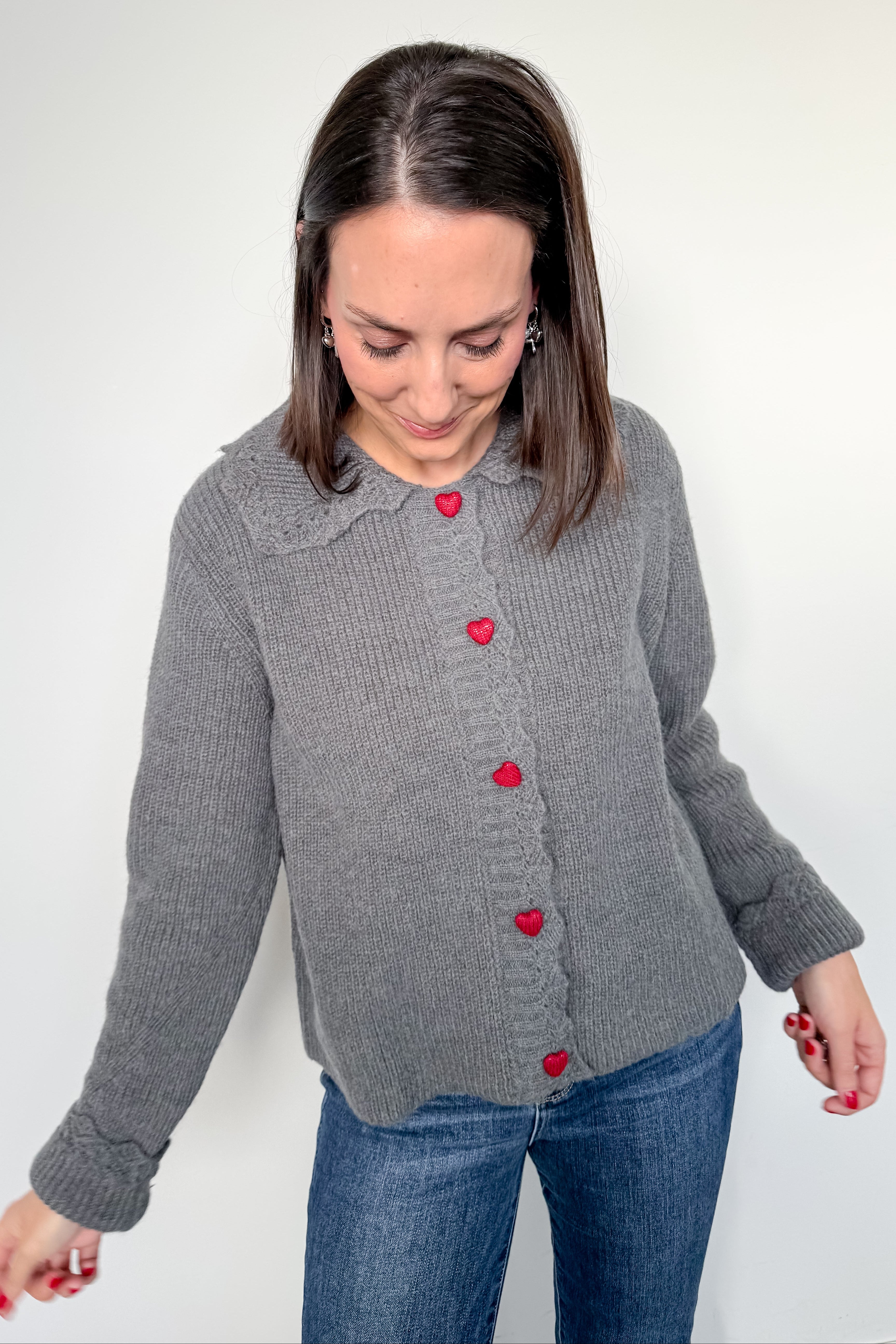 Woman wearing a gray cardigan with red buttons on a white background