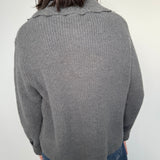 Person wearing a gray sweater and blue jeans on a white background