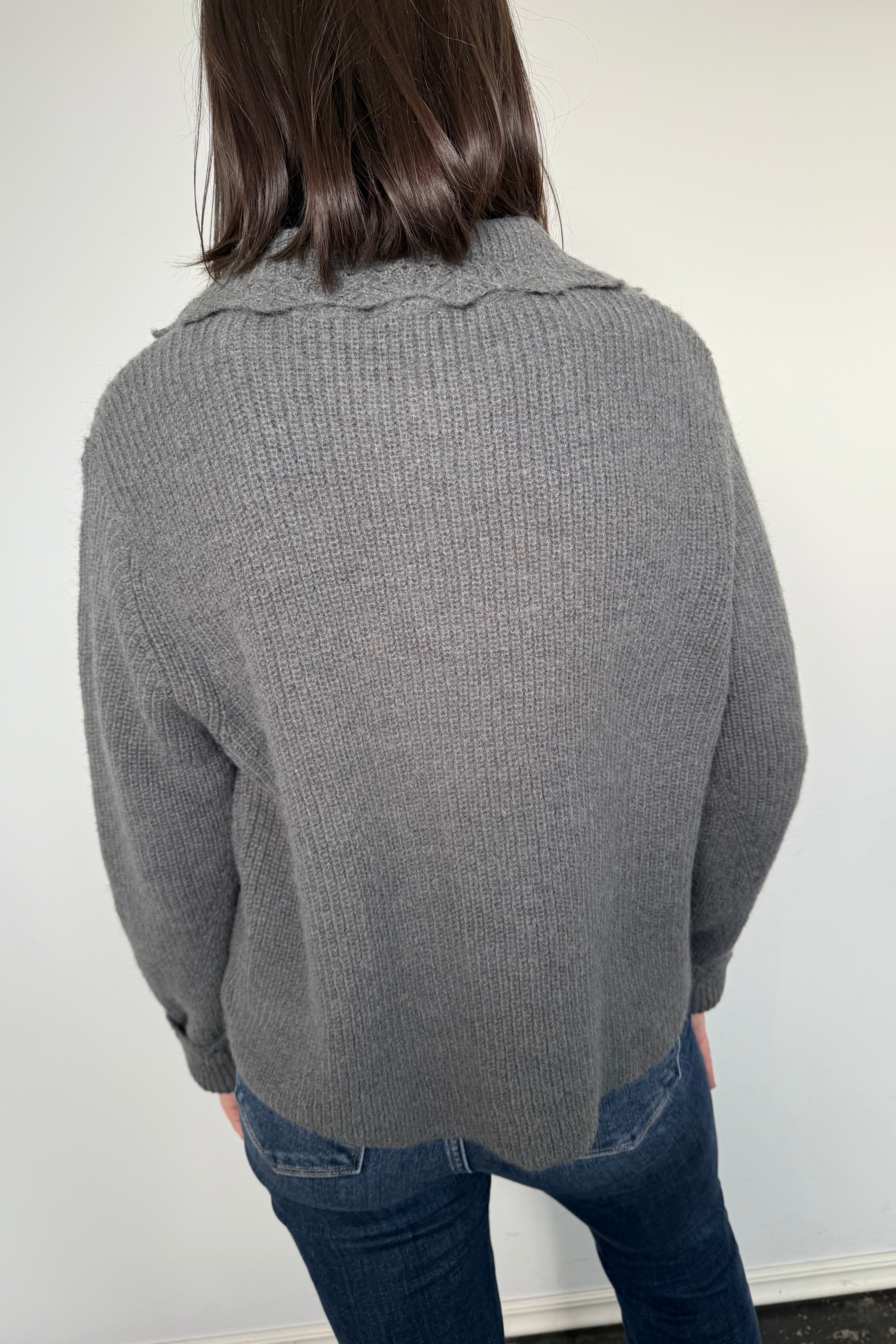 Person wearing a gray sweater and blue jeans on a white background