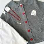 Gray cardigan with red heart buttons on a white surface