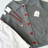 Gray cardigan with red heart buttons on a white surface