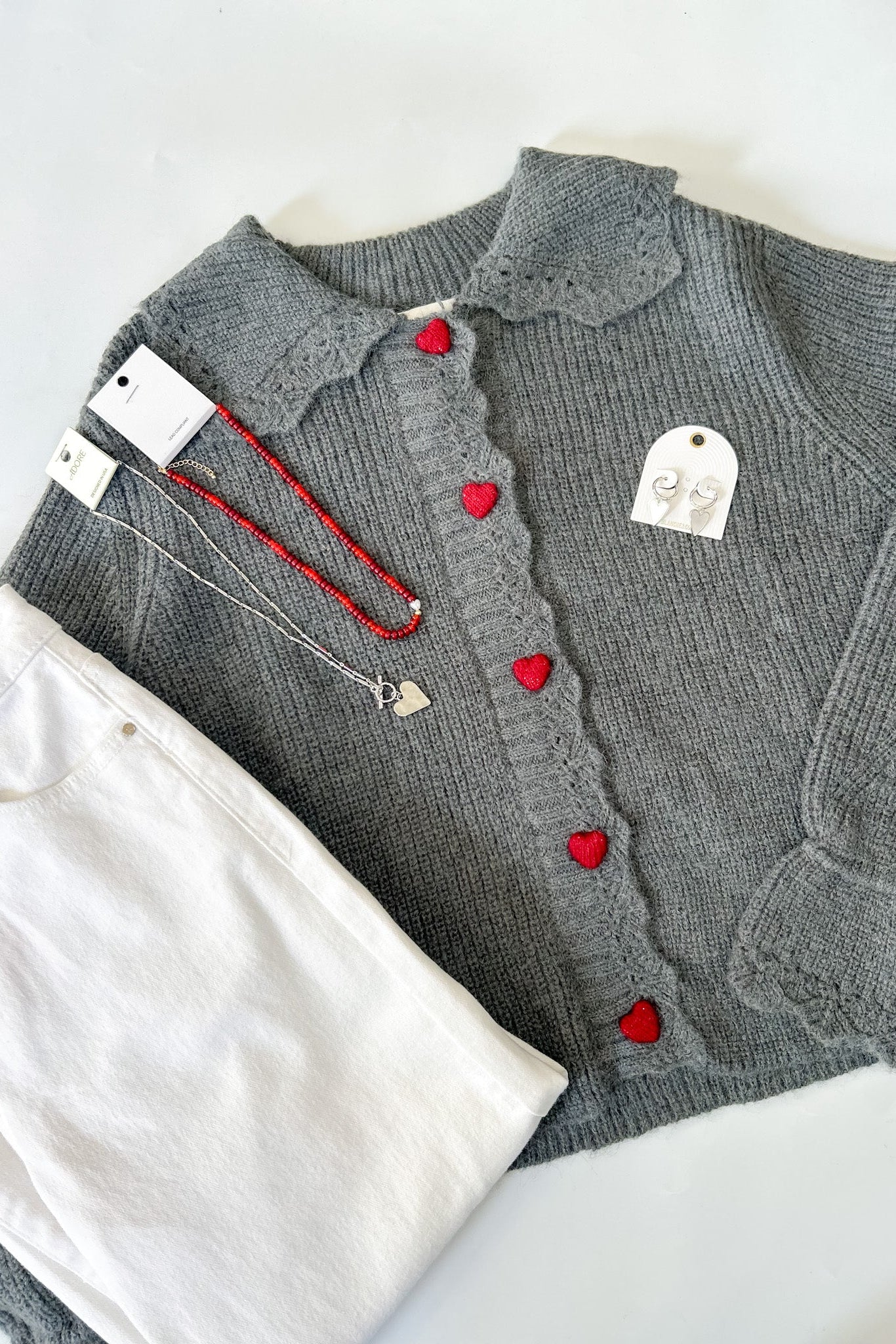 Gray cardigan with red heart buttons on a white surface