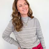 Woman wearing a gray striped sweater and red pants against a white background