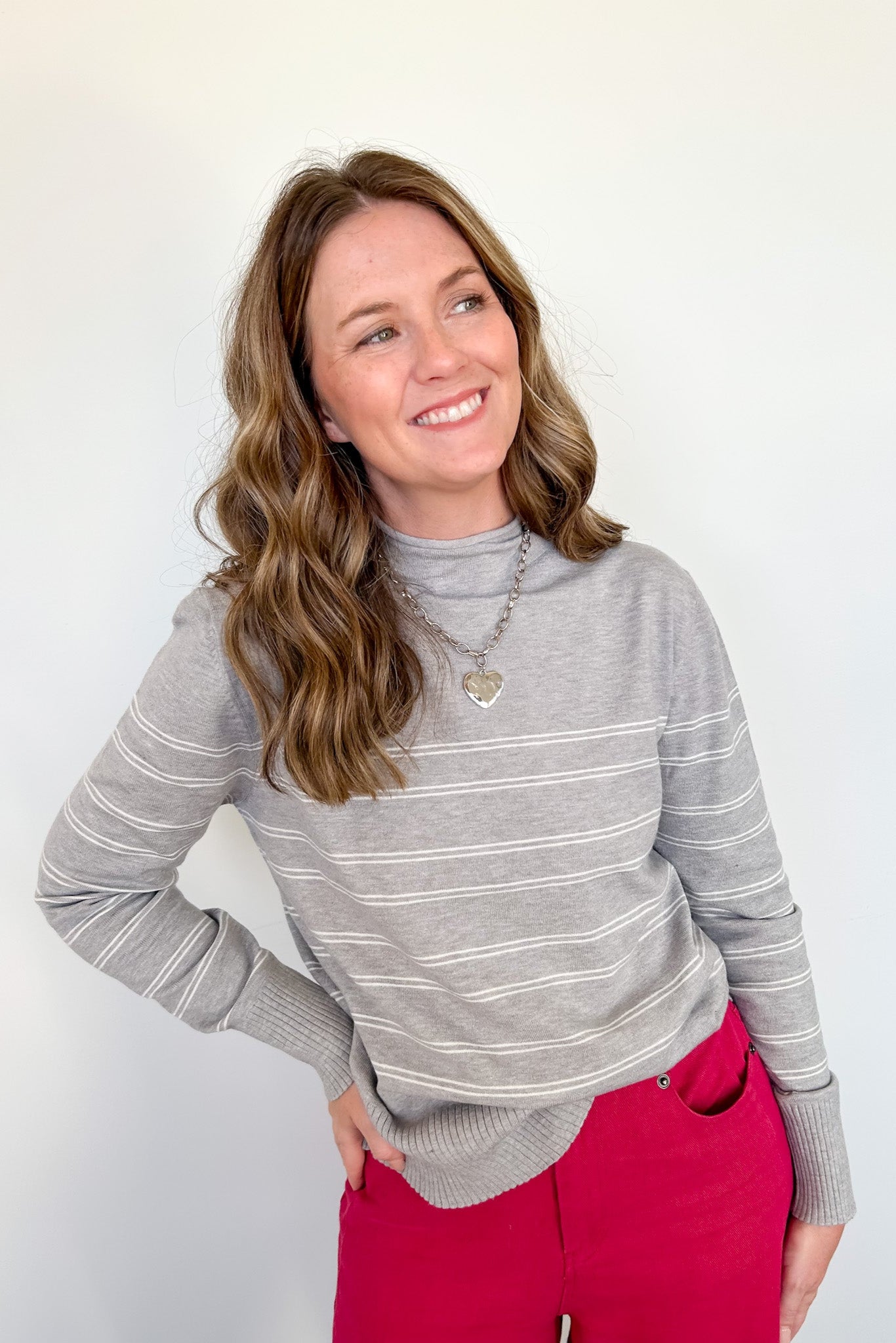 Woman wearing a gray striped sweater and red pants against a white background