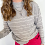 Person wearing a gray striped sweater and pink pants against a white background