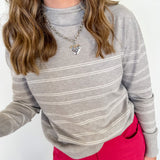 Person wearing a gray striped sweater and pink pants against a white background