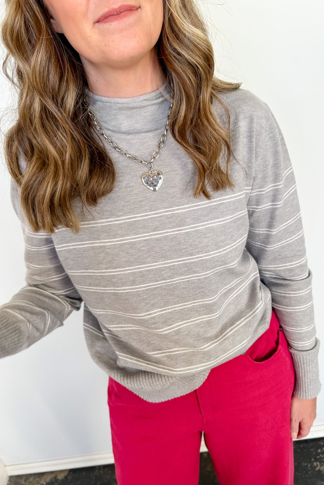 Person wearing a gray striped sweater and pink pants against a white background