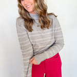 Woman wearing a gray striped sweater and red pants against a white wall