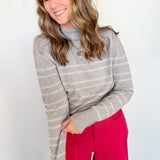 Woman wearing a gray striped sweater and red pants against a white wall