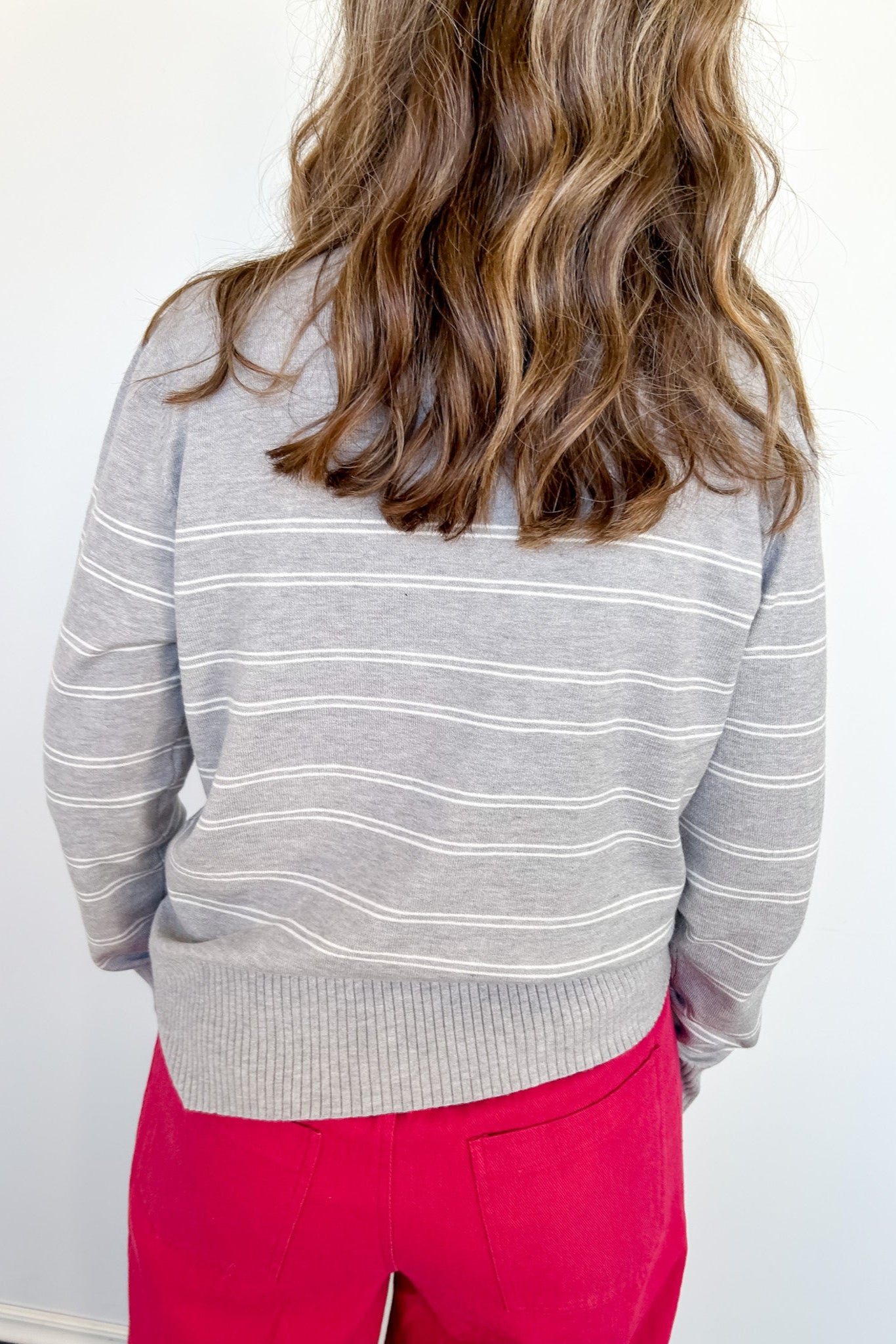 Person wearing a gray striped sweater and red pants against a white background
