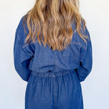 Person wearing a blue denim romper against a white wall