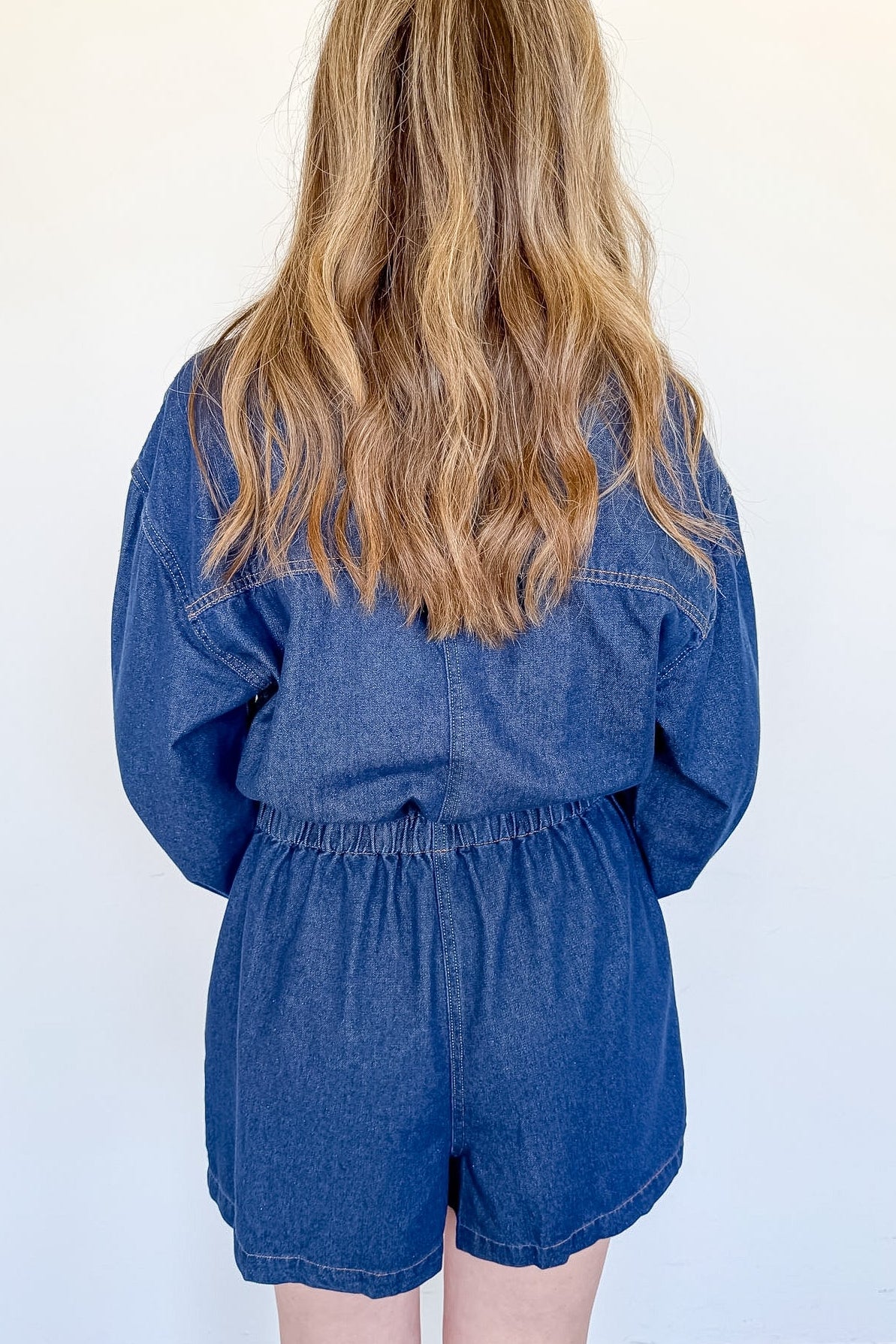 Person wearing a blue denim romper against a white wall