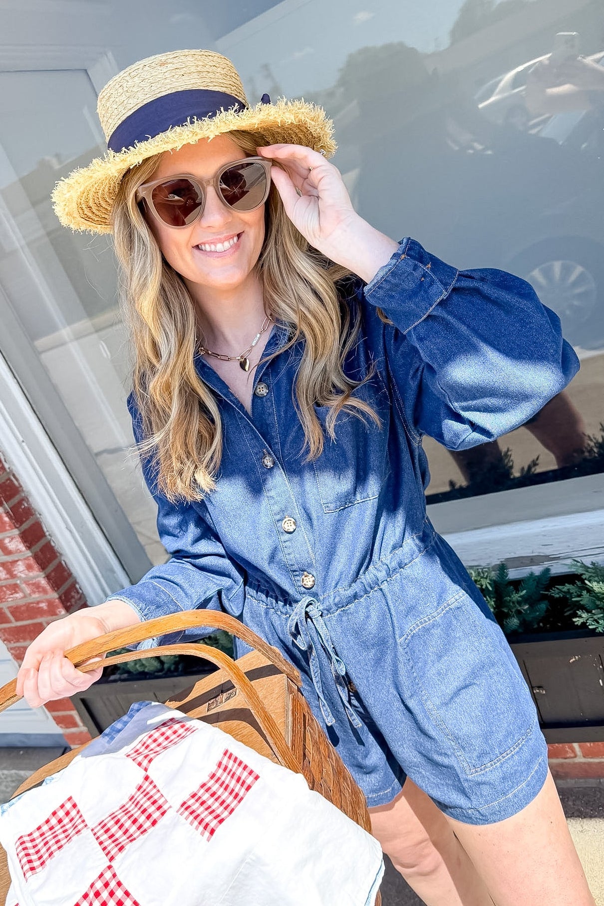 Woman in a denim romper and straw hat holding a basket with a checkered bag.