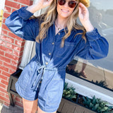 Woman wearing a blue romper and straw hat standing in front of a brick building.