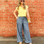 Woman in yellow top and blue jeans standing against a red brick wall.