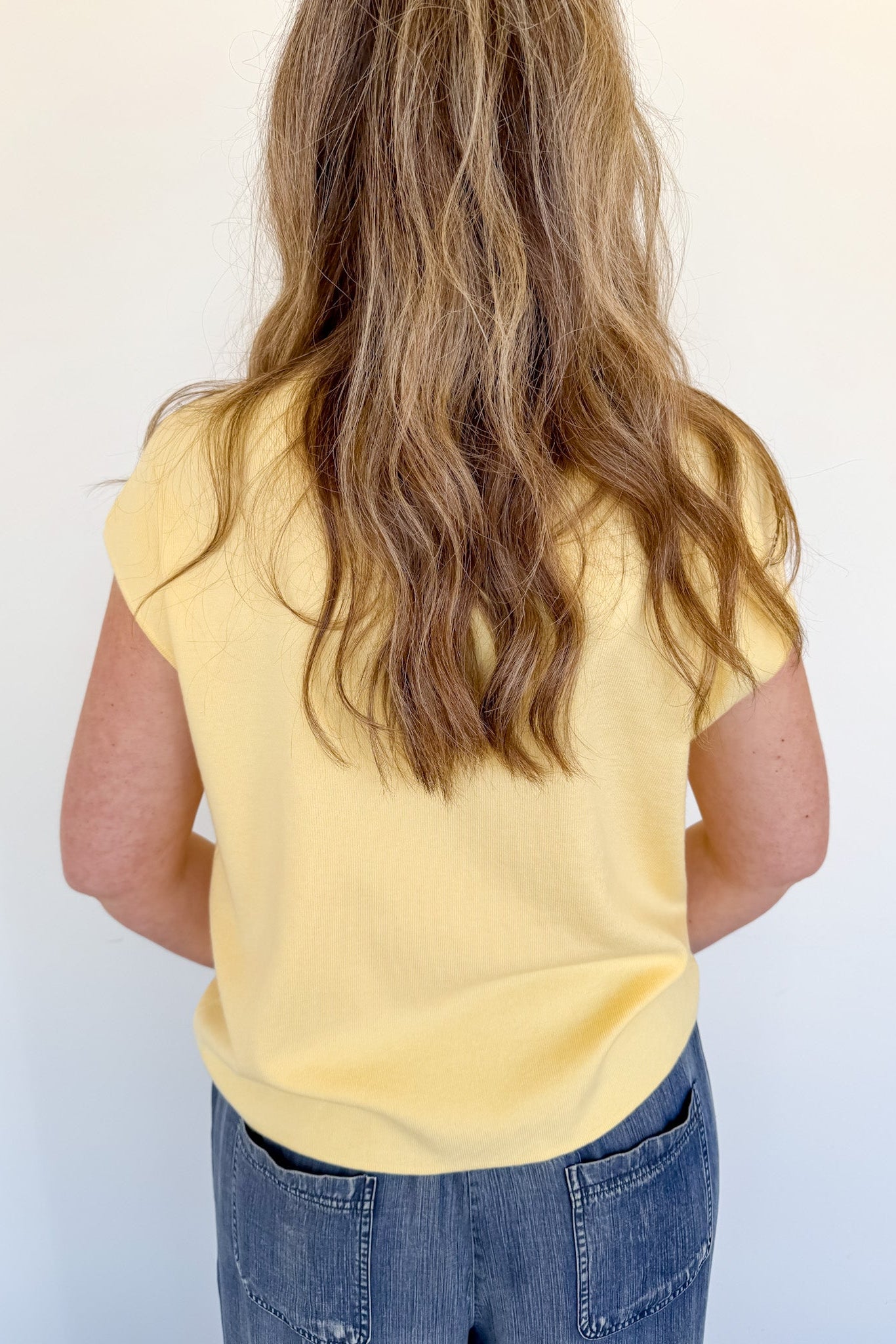 Person wearing a yellow shirt and blue jeans against a white background