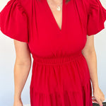 Maxi length dress with v neckline. Short sleeve with slightly bubbled sleeves. Tiered bottom. Elastic waist. Red in color.