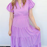 Maxi length dress with v neckline. Short sleeve with slightly bubbled sleeves. Tiered bottom. Elastic waist. Purple in color.