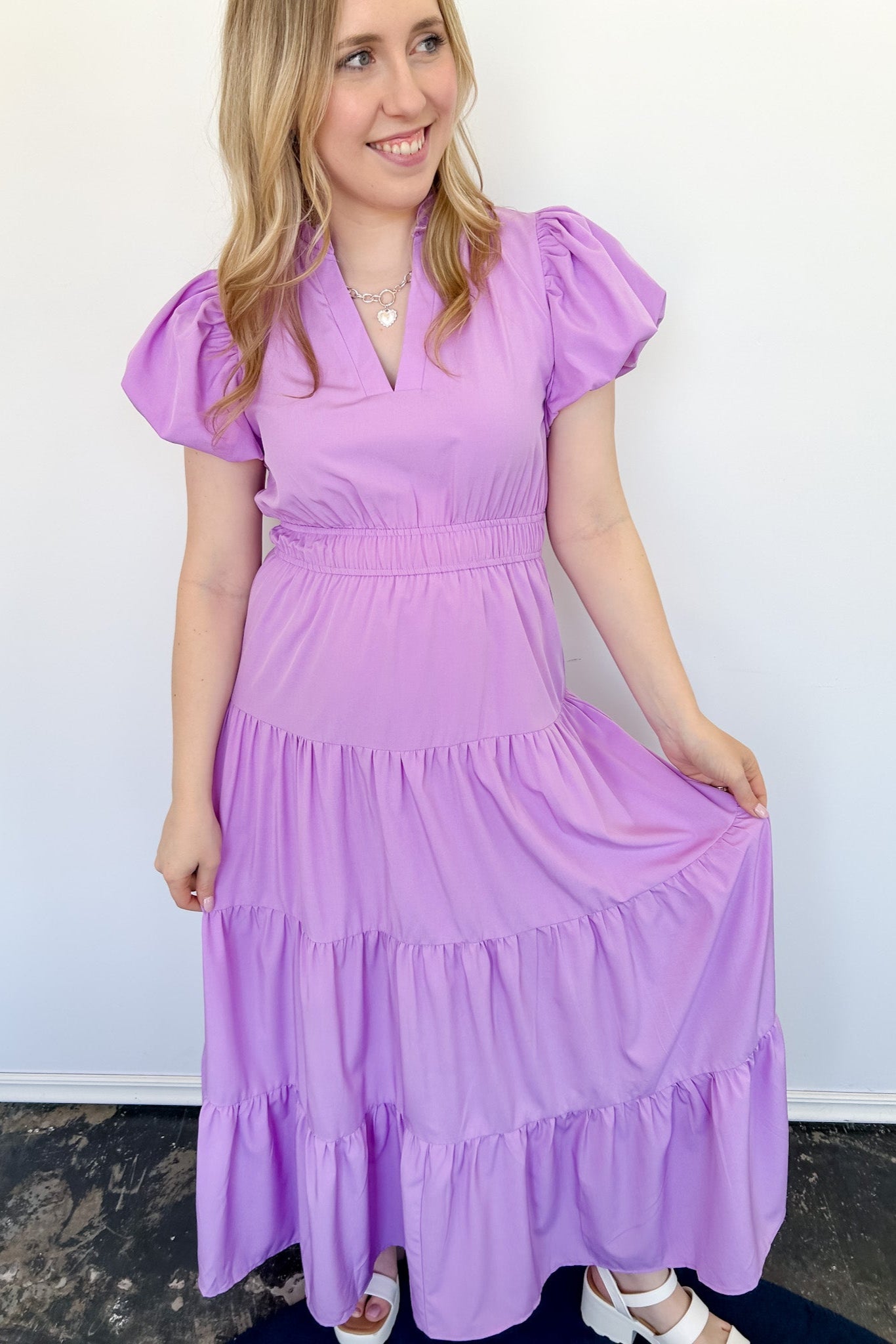 Maxi length dress with v neckline. Short sleeve with slightly bubbled sleeves. Tiered bottom. Elastic waist. Purple in color.